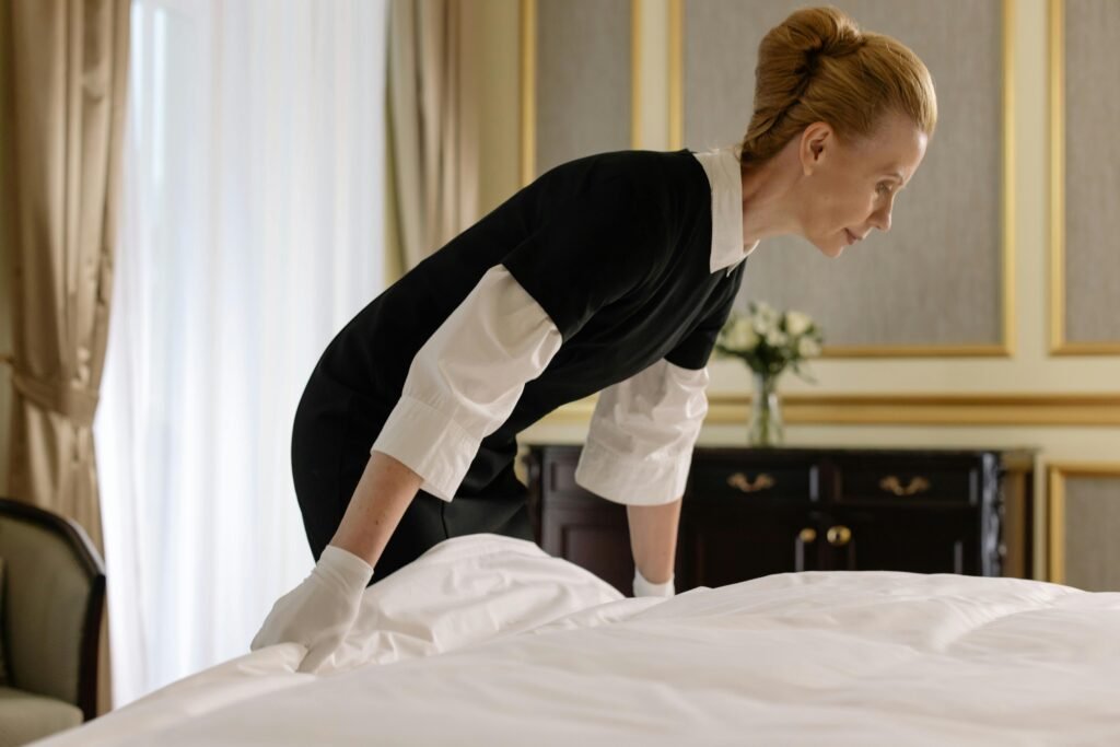pexels-photo-6466493-6466493 Hotel housekeeper making bed in an elegant room, wearing gloves and uniform.